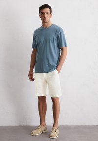 Blaues Baumwoll-T-Shirt, lockere Passform, kombiniert mit cremefarbenen Leinen-Shorts. Helle, lässige Schuhe runden das Outfit ab. Einfaches, sauberes Design.