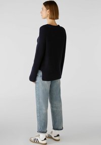 Dunkelblauer gerippter Pullover mit Rundhalsausschnitt, seitlichen Schlitzen und langen Ärmeln, kombiniert mit hellblauen gerade geschnittenen Jeans und weißen Sneakers.