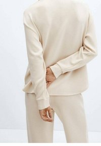 Conjunto de ropa de descanso beige que incluye un top de manga larga con cuello redondo y pantalones a juego, confeccionados con un tejido suave de textura lisa.