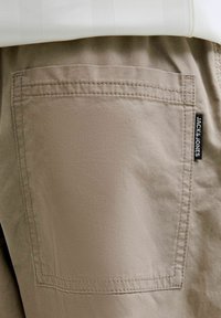 Retro dei pantaloni beige con cuciture visibili e un'etichetta nera del marchio Jack & Jones sul lato destro, indossati con una camicia bianca.