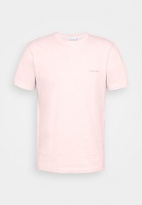 Camiseta de algodón rosa claro con mangas cortas, cuello redondo, que presenta un sutil logo de "Calvin Klein" bordado en el lado izquierdo del pecho.
