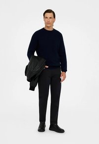 Tamsiai mėlynas megztinis, lieknos juodos kelnės ir juodi odiniai aulinukai. Modelis laiko juodą odinę striukę, neutrali fono spalva.