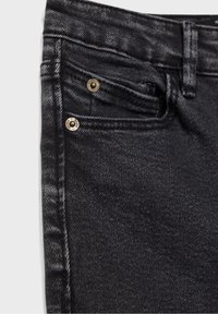 Acercamiento de un bolsillo de jeans de mezclilla negra con remaches metálicos y costura visible en la tela texturizada.