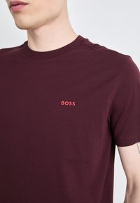 Bordový bavlněný tričko s kulatým výstřihem a krátkými rukávy, s kontrastním červeným vyšitým logem "BOSS" na hrudi.
