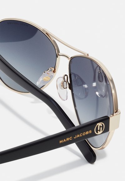 Goldene Metall-Fliegerbrille mit dunklen Verlaufslinsen, schwarzen Kunststoffbügeln mit Logo und durchsichtigen Nasenpads für zusätzlichen Komfort.