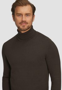 Pull à col roulé marron au design ajusté, présentant un col à côtes et une texture lisse. Le matériau semble être un tricot doux et léger.