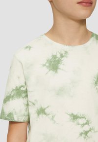 Weißes T-Shirt mit kurzen Ärmeln und grünem Batikmuster, runder Ausschnitt und weichem Baumwollstoff. Sichtbare Nahtdetails an den Ärmeln.