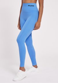 Blå högmidjade leggings tillverkade av stretchigt material, med en texturerad design och kontrasterande rosa sömmar, i kombination med vita sneakers.