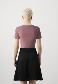 Kratší rukáv, přiléhavý top v barvě mauve zkombinovaný s černou nabíranou sukní, která má hladkou texturu a střední délku.