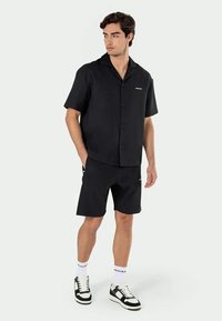Camisa preta de manga curta com um design de colarinho, combinada com calções a condizer. Tecido texturizado com um pequeno detalhe de logótipo, complementado por ténis.