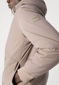 Svijetlosmeđi dukserica s kapuljačom, elastičnim manžetama i prsnom džepom s kvadratnom oznakom BOSS. Teksturirani materijal, elegantan dizajn.