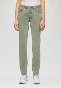 Hellgrüne Denim-Jeans im slim fit mit einem Fünf-Taschen-Design, Gürtelschlaufen und einer glatten Textur. Kombiniert mit klobigen grau-weißen Sneakers.