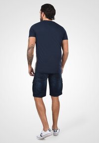Camiseta azul marino de manga corta, combinada con pantalones cortos cargo de mezclilla oscura. Los pantalones cortos cuentan con bolsillos laterales y un corte relajado. Zapatillas blancas completan el look.