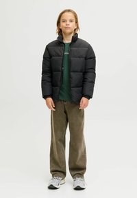 Svart dunjakke med høy krage, quiltet mønster, brukt over en grønn skjorte. Kombinert med løse khakibukser og grå joggesko.