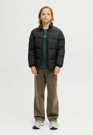 Must pufferjope kõrge kraega, tikitud mustriga, kantud rohelise särgi peal. Sobitatud lahtiste khaki-pükstega ja hallide tossudega.