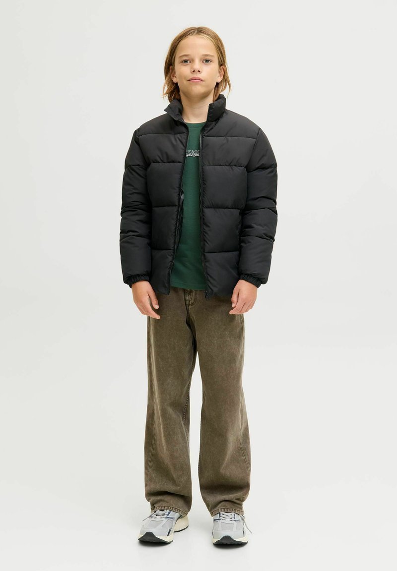 Svart dunjakke med høy krage, quiltet mønster, brukt over en grønn skjorte. Kombinert med løse khakibukser og grå joggesko.