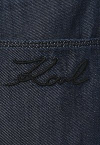 Τζιν ύφασμα σε σκούρο μπλε χρώμα με κεντημένη υπογραφή "Karl" σε μαύρη κλωστή κατά μήκος της ραφής.