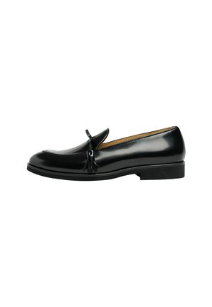 Mocassin en cuir noir avec détail pompon, talon bas et finition lisse et polie, vu de profil sur fond blanc.