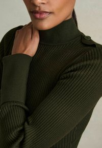 Dunkelgrüner, gerippter Rollkragenpullover mit taillierter Passform, der mit Knopfdetails an der Schulter und strukturiertem Stoff an den Ärmeln ausgestattet ist.