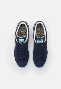 Námornícke semišové tenisky s bielymi podrážkami a šnúrkami. Zelené logo Puma na jazyku, zlaté detaily na boku, vzorovaná vnútorná vložka s brandingom Puma.