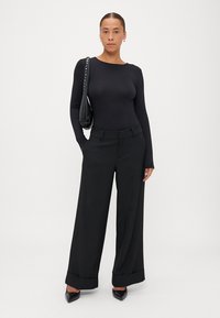 Melnā pieguļošā garām piedurknēm augšdaļa saskaņota ar platām melnām biksēm ar salocītām apakšmalām. Aksesuārs ir melna soma ar sudraba kniedēm.