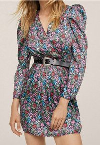 Blumengemustertes Kleid mit Puffärmeln, einem taillierten Oberteil und einem schwarzen Gürtel mit dekorativer Hardware. Der Hintergrund ist einfarbig.