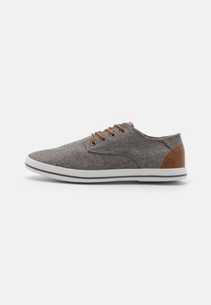Sneaker in tessuto grigio con accenti in pelle marrone, punta rotonda, suola in gomma bianca e cinque occhielli marroni per i lacci. Design leggero e informale.