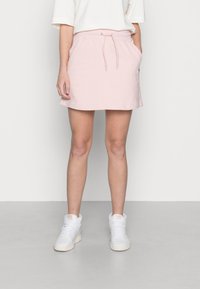 Jupe en sweat rose clair avec une taille élastique, un cordon de serrage et des poches latérales, associée à des baskets montantes blanches.