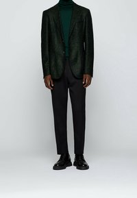 Mörkgrön, strukturerad blazer över en matchande polotröja, i kombination med svarta byxor och blanka svarta skor, med en klassisk passform.