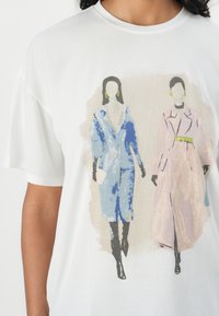 White t-shirt featuring a graphic print of two figures in blue and pink outerwear, with black boots and green accessories. Soft texture.