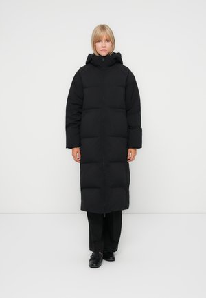 Black long puffer coat with a zip closure, hood, and large sections creating a quilted texture. Features wide sleeves and a straight fit.