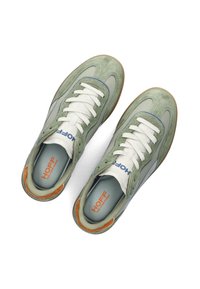 Zapatillas de ante y cuero verde con cordones blancos. Presentan un acento azul en el lateral y un logo naranja en la plantilla. Suela de goma.