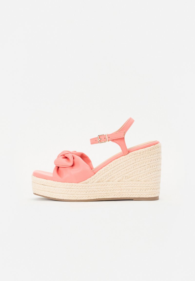 Coral wedge sandal with fabric bow detail. Features a woven straw platform and ankle strap. Smooth finish and open toe design.