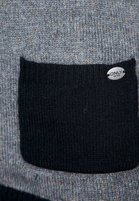 Maglione grigio a maglia con una tasca nera e un'etichetta argentata. Il materiale presenta sottili sfumature di colore in tutto il capo. Tessuto strutturato.