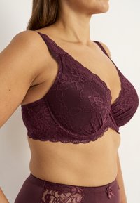 Spitzen-BH in dunklem Burgunderrot mit floralem Muster. Verfügt über verstellbare Träger und gewellte Kanten. Glatte Textur mit Unterdrahtunterstützung.