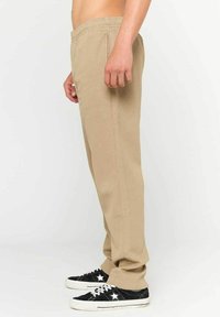Beige chinos med elastisk talje, lige ben-design og sidelommer, båret med sorte sneakers med hvide accenter.