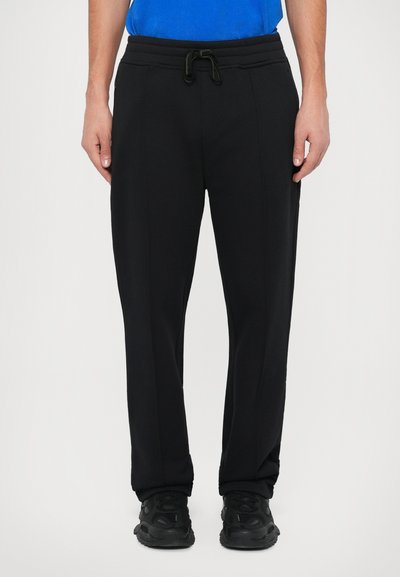Schwarze Jogginghose mit einem Kordelzugbund, zwei Taschen an den Seiten und einem schmal zulaufenden Design. Der Stoff wirkt glatt mit einem leicht schimmernden Finish.