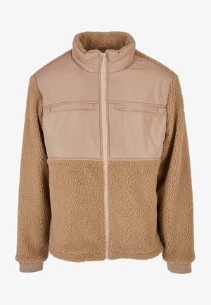 Veste en polaire beige avec des panneaux supérieurs lisses. Fermeture éclair intégrale, col haut, deux poches poitrine et corps texturé pour plus de chaleur.
