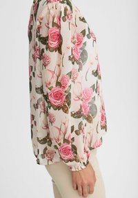 Blumenbluse mit langen, puffierten Ärmeln. Hergestellt aus leichtem, durchscheinendem Stoff mit einem rosa Rosenmuster auf einem cremefarbenen Hintergrund. Geraffte Manschetten.