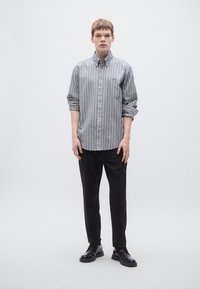 Szürke és fehér csíkos, gombos hosszú ujjú ing, felhajtott ujjakkal, fekete nadrággal és fekete cipővel párosítva, minimalista dizájn.