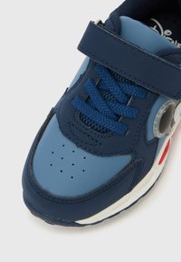 Pantof sport albastru pentru copii, cu șireturi albastre, o bandă cu Velcro, talpă albă cu accente roșii și mici găuri de ventilație în zona degetelor.