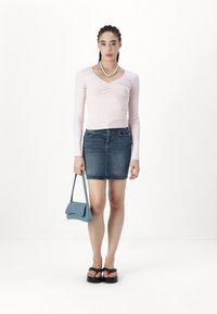 Lys rosa langermet topp med samlet hals, kombinert med et tettsittende blått denimskjørt og en liten blå håndveske. Svart platå sandaler.