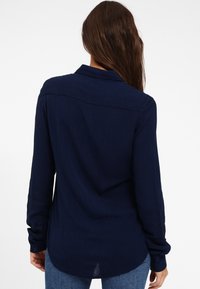 Granatowa koszula z długim rękawem w poziome paski, z guzikami przy mankietach i zaokrąglonym dołem, uszyta z lekkiego materiału.