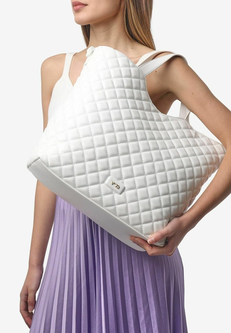 Sac à main blanc matelassé avec une forme asymétrique unique, présentant une texture lisse et un accent logo métallique à l'avant.