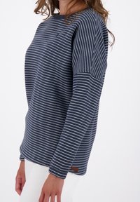 Felpa a righe blu navy con strisce bianche, colletto rotondo e tessuto testurizzato. Presenta un piccolo logo e un'etichetta in tessuto sul lato.