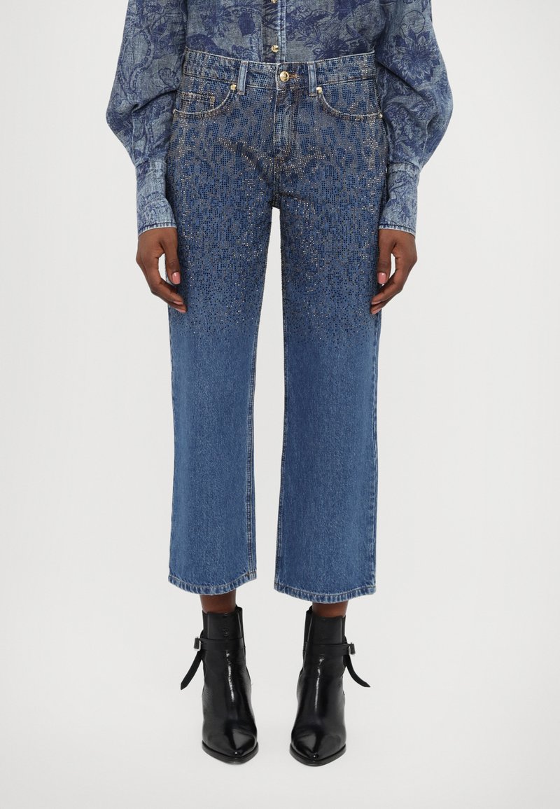 Light blue denim jeans with a relaxed fit, featuring a gradient of small metallic studs near the bottom. Finished with a straight cut and frayed hem.