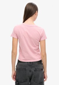 Rosa Baumwoll-T-Shirt mit Rundhalsausschnitt und kurzen Ärmeln, mit einer figurbetonten Passform und einem kleinen roten Etikett auf dem linken Ärmel.