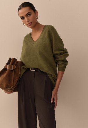 Olive green V-neck sweater made of soft fabric, paired with brown high-waisted trousers and a brown suede handbag. Simple, relaxed fit.