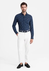 Marineblauw overhemd met knopen en een tonale bloemenpatroon, gecombineerd met witte broek en zwarte instappers. Heeft een kraag en een aangesloten ontwerp.