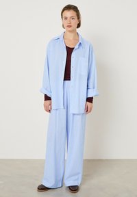 Šviesiai mėlyna dryžuota didelio dydžio marškiniai, derinami su atitinkančiomis plačiomis kelnėmis. Marškiniai turi krūtinės kišenę ir sagas, dėvimi per bordo spalvos viršutinį drabužį.